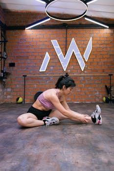 Athletic woman performing a floor stretch in a modern gym with brick walls and industrial design.