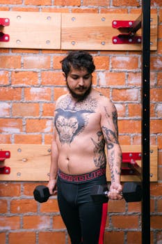 A shirtless tattooed man lifting dumbbells in a gym. Fitness and strength concept.
