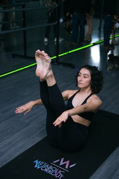 A focused woman in an athletic pose on a yoga mat inside a modern gym setting.