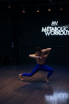 A man dynamically dancing shirtless in a neon-lit gym studio, showcasing muscular moves.