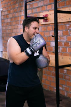 Smiling young male boxer wearing gloves, training in a boxing gym with a playful mood.