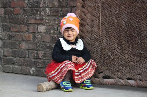 Free Cute young girl in a vibrant red skirt and a beanie, sitting with eyes closed outside in Bijnor, India. Stock Photo