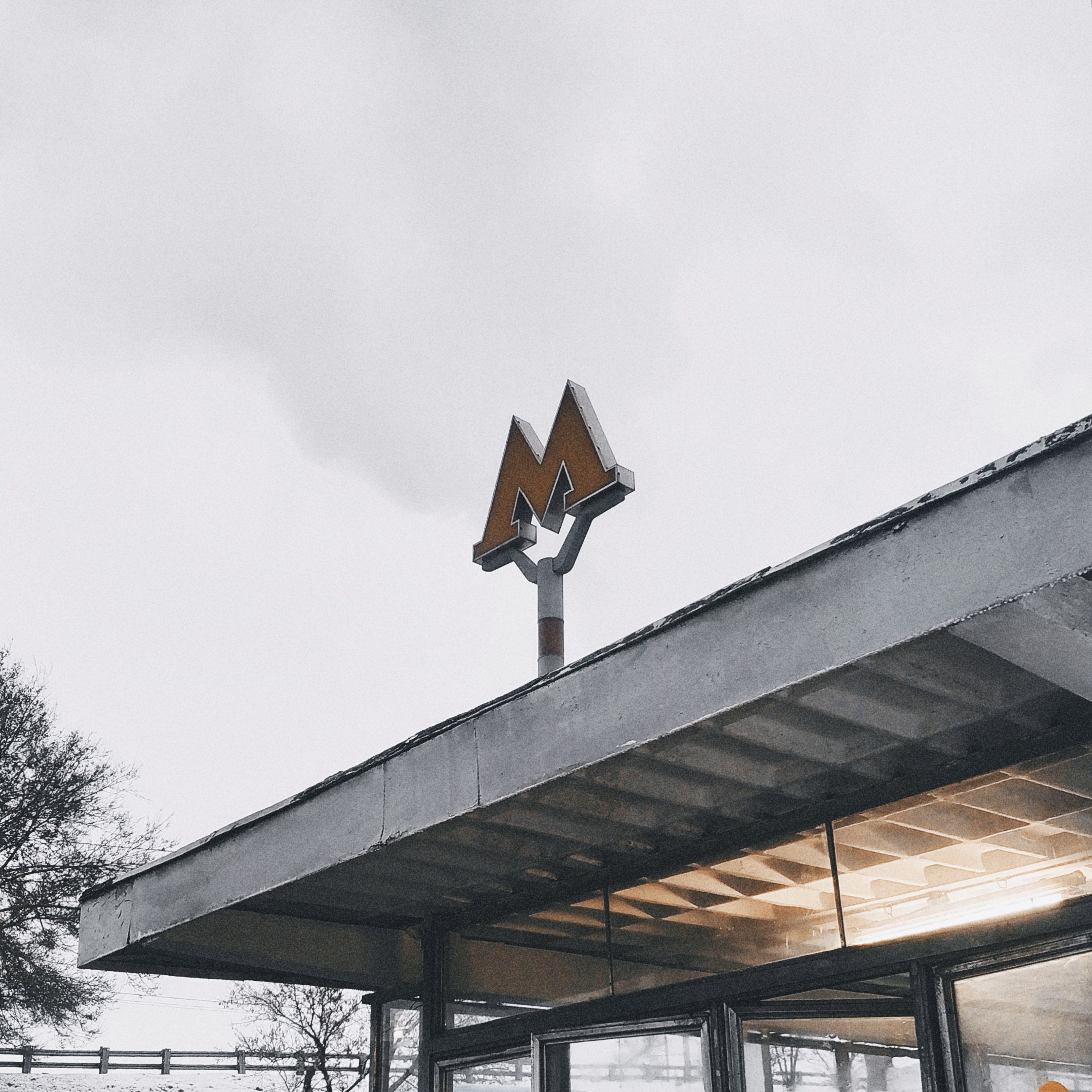 A modern subway station entrance featuring a distinct metro logo on a cloudy day.