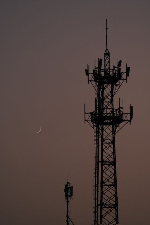 Free Silhouette of a telecommunication tower at dusk with a crescent moon in the background. Stock Photo