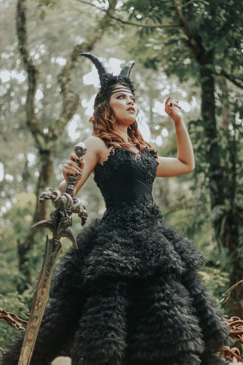 Free A woman in an ornate black gown poses with a sword in a lush outdoor setting, exuding fantasy vibes. Stock Photo
