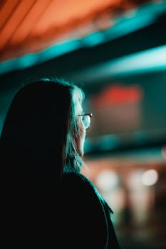 Silhouette of a woman with glasses in a colorful night street scene in Liège, Belgium.