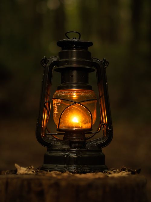 Free A close-up of a vintage oil lamp glowing warmly in a serene forest at night. Stock Photo