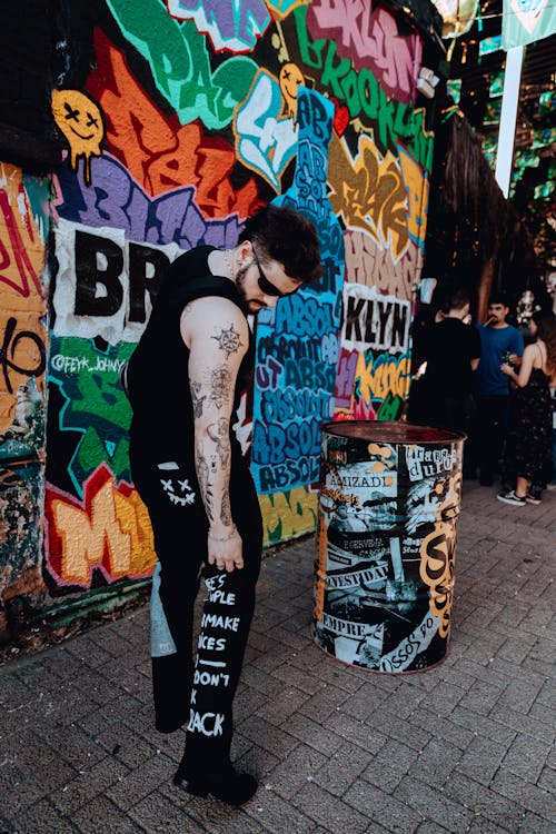 Photo of a Young Man in a Black Tank Top Standing in front of a Graffiti Wall