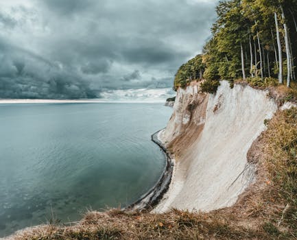 A stunning view of a dramatic coastal cliff overlooking the calm sea and cloudy sky.