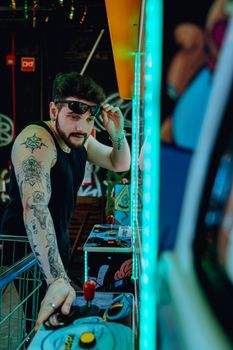 Tattooed young man in a casual style playing retro arcade games indoors. Urban fun vibe.