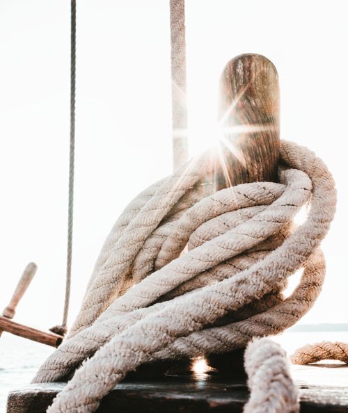 Free Close-up of sunlit rope coiled around a wooden mast on a boat, capturing nautical adventure. Stock Photo