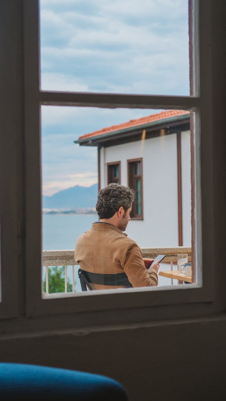 View From Window On Man Sitting On Outdoor Terrace