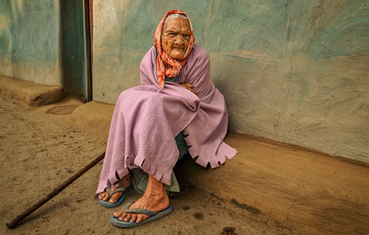 Elderly Woman Wearing Headscarf Sitting On Ground
