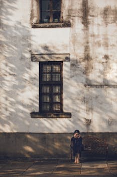 Woman seated on a bench against a textured wall, shadows creating a calming atmosphere.