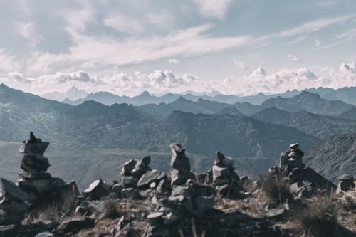 Free Serene view of rock cairns stacked against a vast mountain range with cloudy skies. Stock Photo