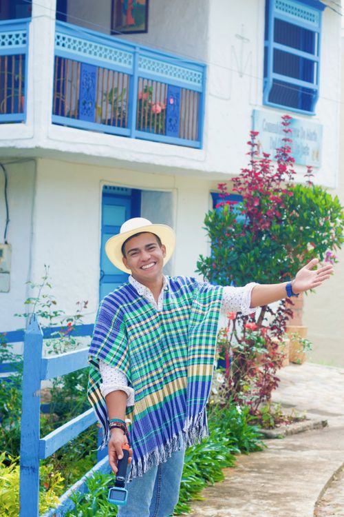 Free Happy man in a vibrant poncho and hat, gesturing outdoors by a traditional building. Stock Photo