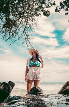 A woman stands joyfully on a rocky beach in Cartagena, Colombia, under a vibrant sky.