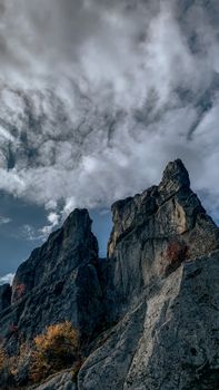 Vertical shot of towering rocks against a moody sky with white clouds, creating a dramatic and natural scene.