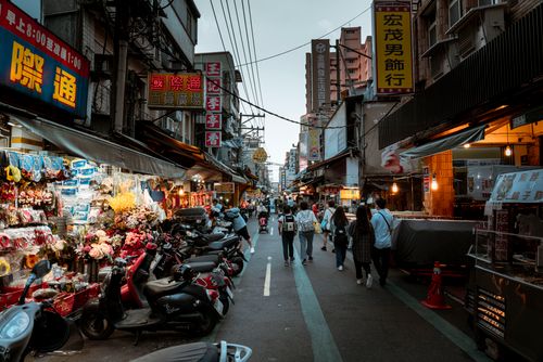 Free Bustling Asian city street scene with shops, pedestrians, and scooters in a lively urban shopping district. Stock Photo