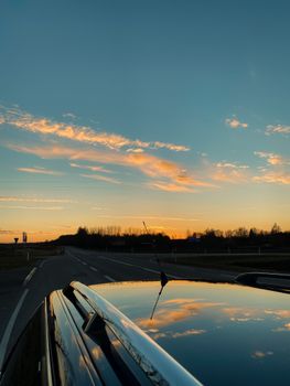 A serene sunset reflects on a car roof along an open road, highlighting a peaceful evening drive.