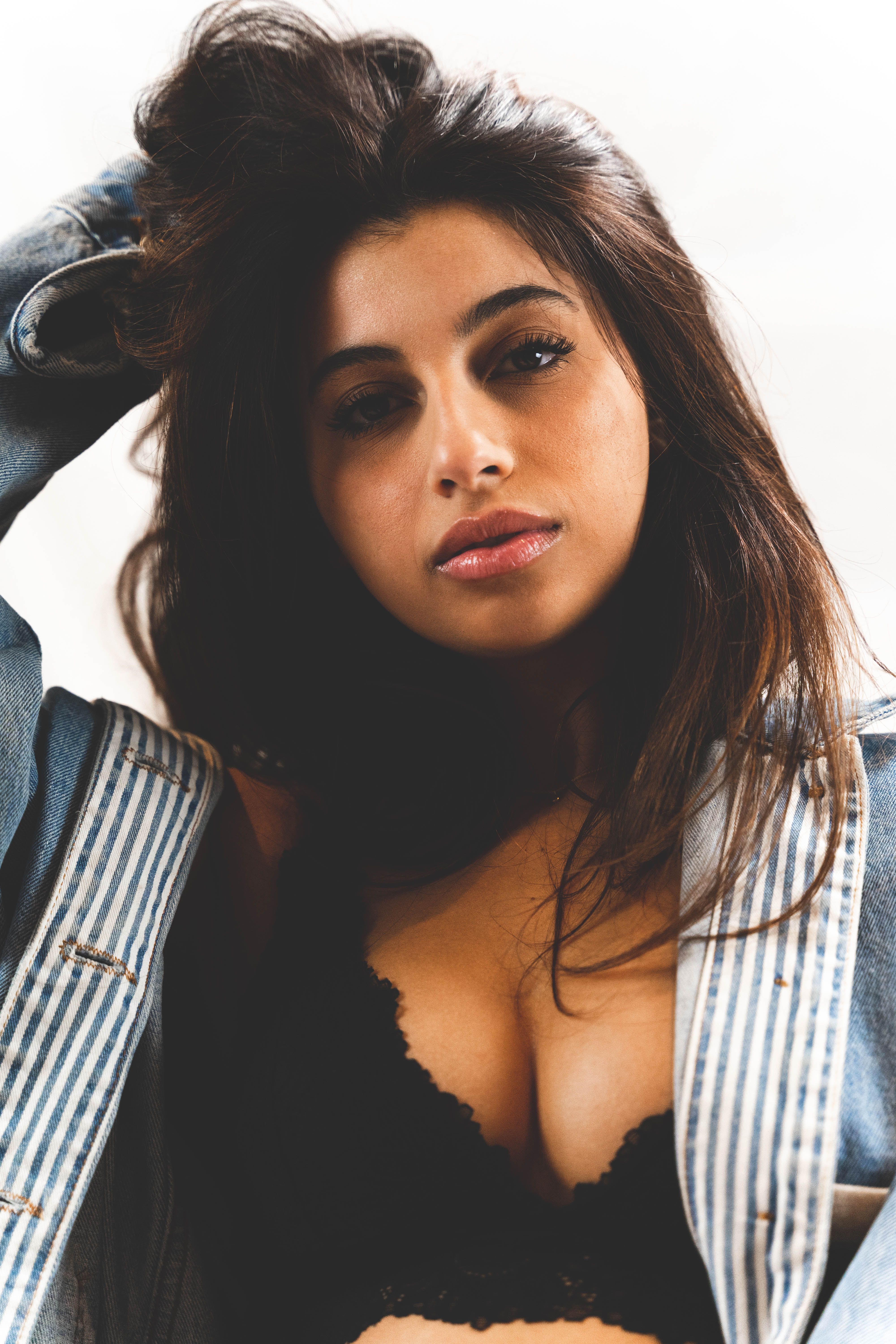 A fashionable young woman poses confidently in a studio, wearing a denim jacket and black bra.