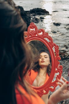 A woman holding a red mirror reflects her image against a scenic Turkish beach.