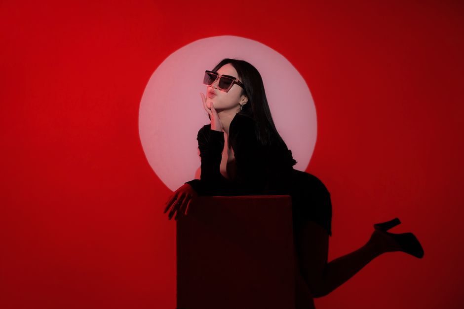 Woman in sunglasses posing against a bold red background with dramatic lighting.