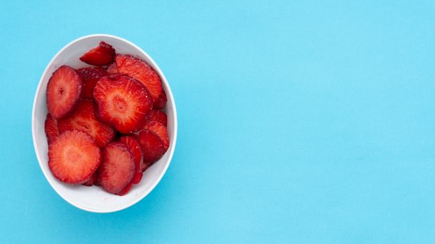 A bowl filled with fresh sliced strawberries on a bright blue background.