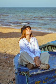 Woman sitting on a boat at the beach, smiling with eyes closed, enjoying the peaceful setting.