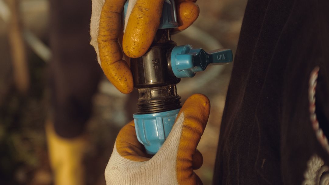 A worker's gloved hands assembling a water pipe outdoors