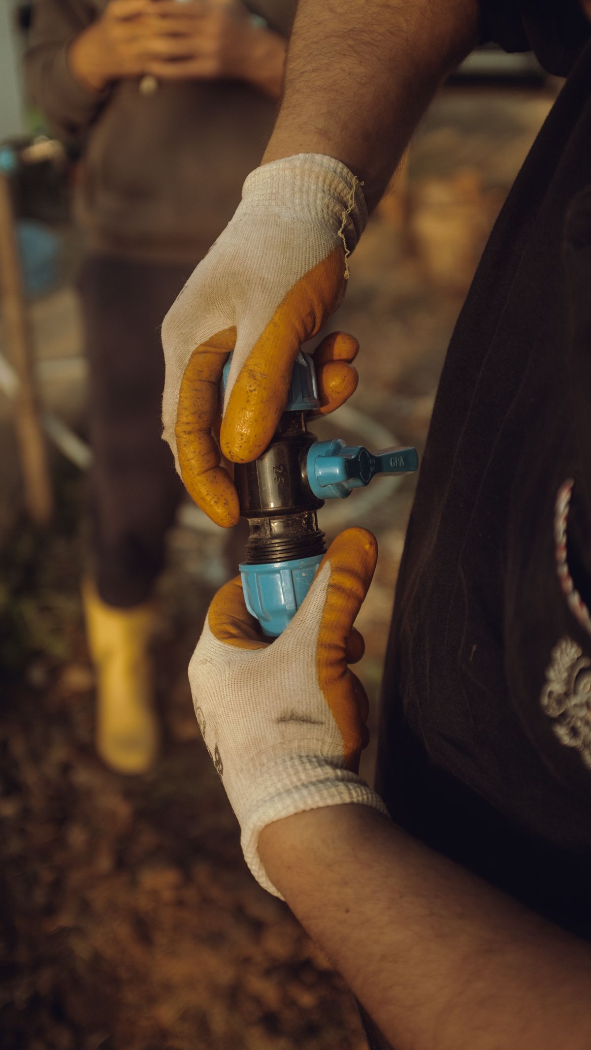 Worker in gloves fitting a blue compression coupling onto a black HDPE pipe during outdoor installation