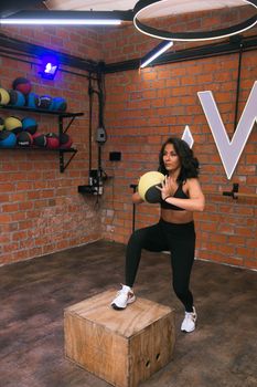 A woman working out with a medicine ball in a modern gym with exposed brick walls in Ciudad de México.