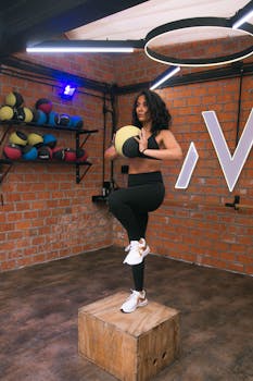 Woman practicing a balance exercise with a medicine ball in an urban gym setting in Ciudad de México.