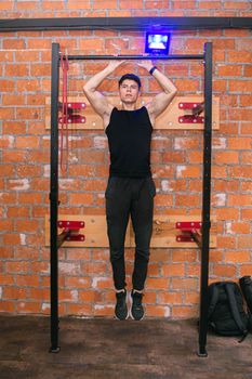 Muscular man demonstrating pull-up exercise indoors against a brick wall.