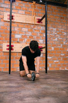An adult male performing an ab roller exercise in a modern gym with brick walls.