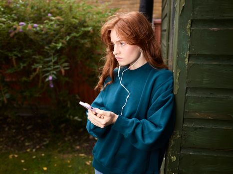 Woman Leaning against Shed Listening to Music from Phone