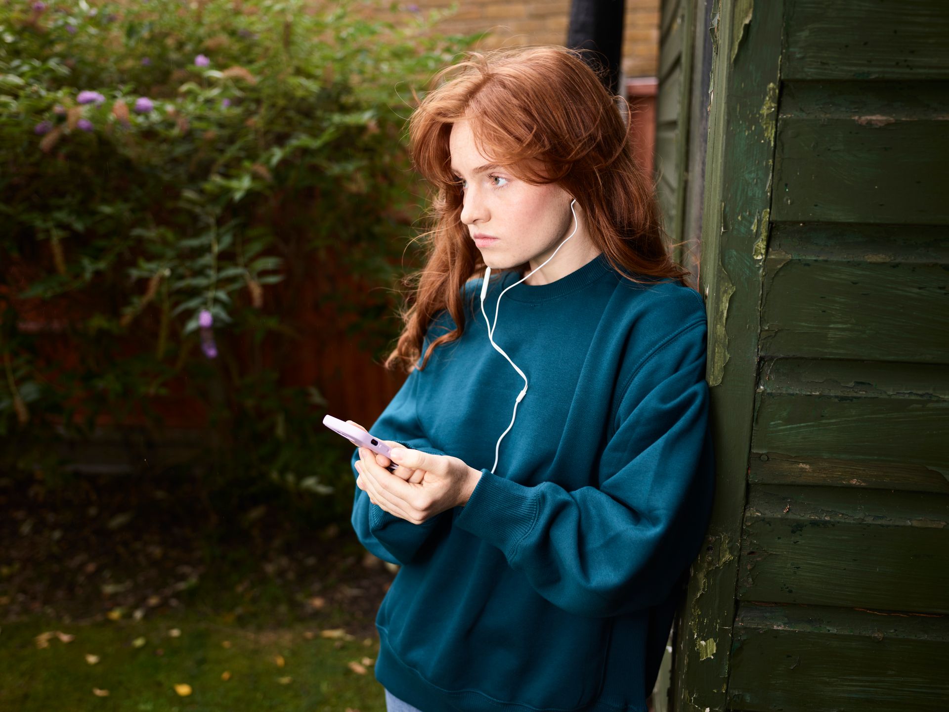 Woman Leaning against Shed Listening to Music from Phone