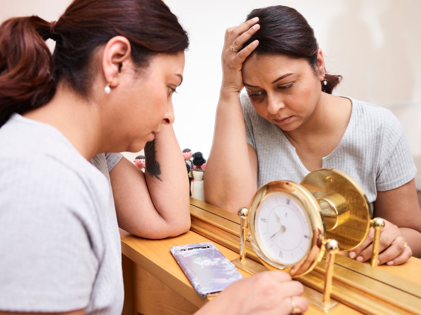 A woman looks pensive and tired, reflecting on burnout with a clock and mirror.