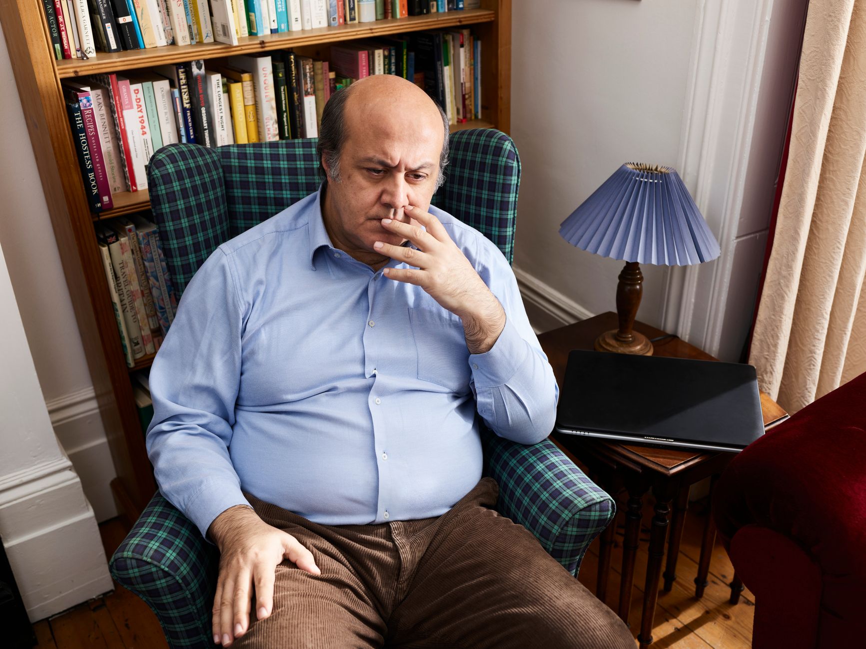 Middle-aged man seated in a home library, lost in thought, signifying digital disconnection.