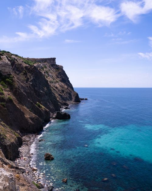 Free A stunning view of a rocky cliffside against a bright blue ocean under a clear sky. Stock Photo