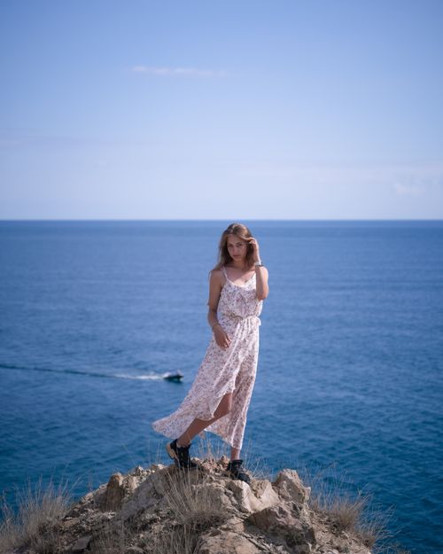 Free A woman poses elegantly in a white dress on a cliff overlooking the ocean. Stock Photo