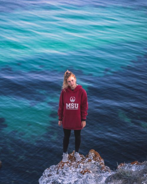 Free Blonde woman in sweatshirt stands on cliff overlooking the sea. Adventure and freedom in nature. Stock Photo