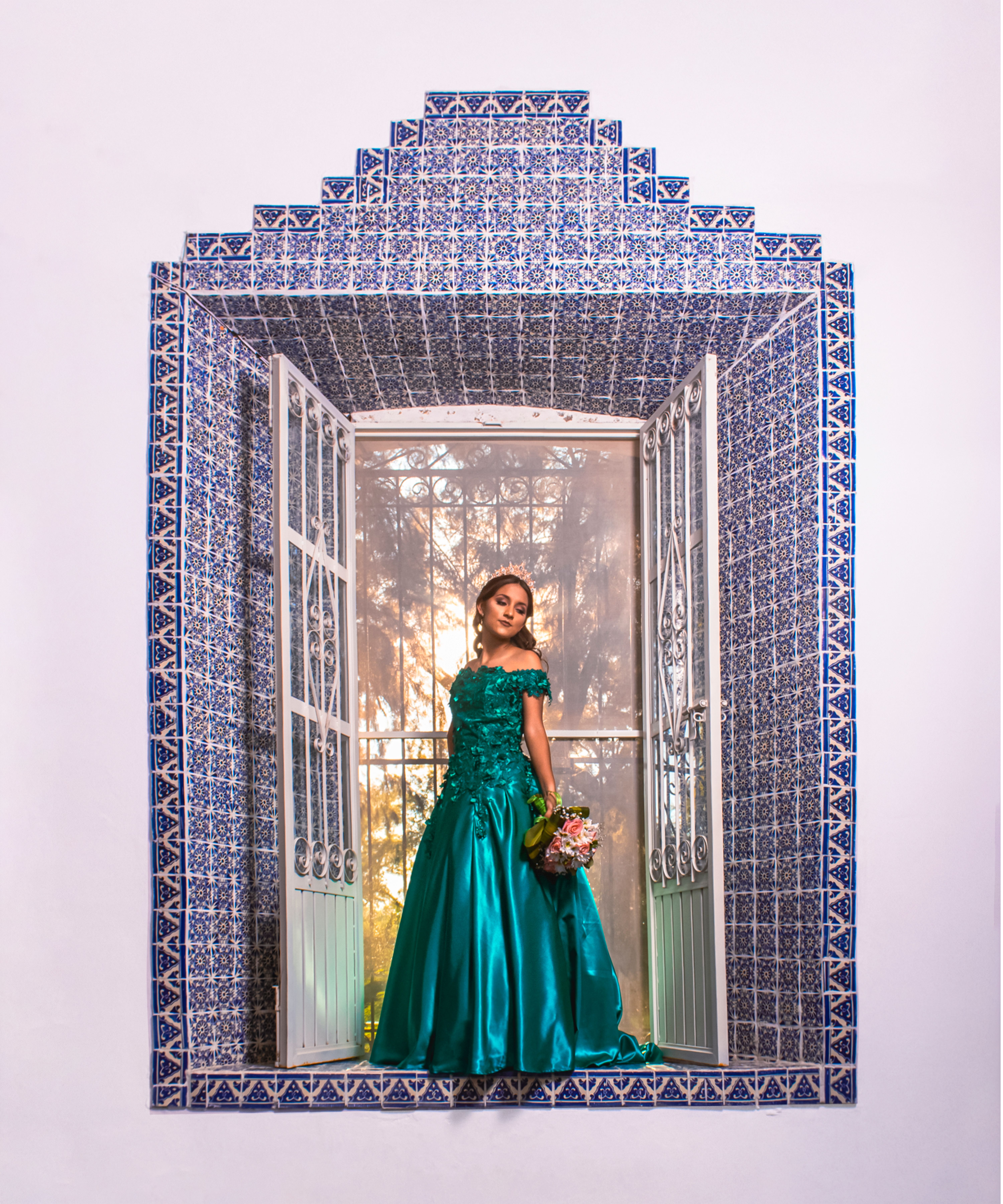 A woman elegantly posing in a turquoise gown, framed by a stunning mosaic window design.