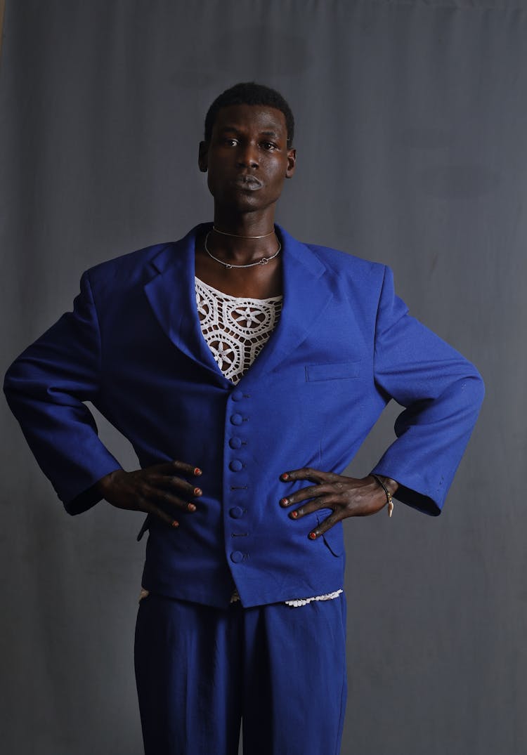 A Man Wearing Blue Blazer And Pants Standing Near Gray Wall While Hands Is On His Waist