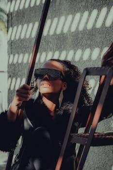 A modern woman wearing sunglasses poses against a patterned wall.