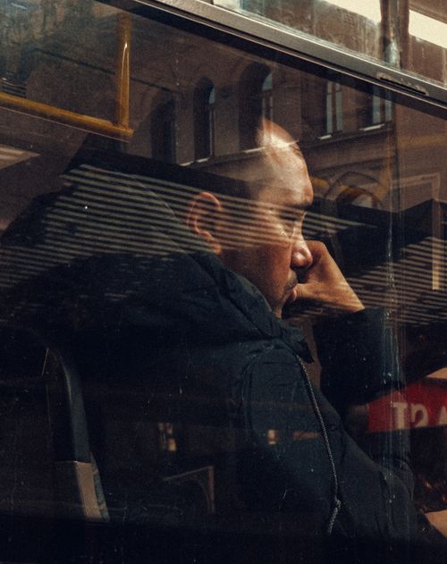 Free Man sitting on a bus, reflecting through windowpane during city transit journey. Stock Photo