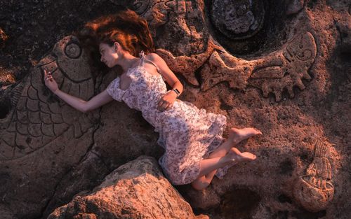 Free A woman in a printed dress lies gracefully on ancient carved rocks, captured from a top view. Stock Photo