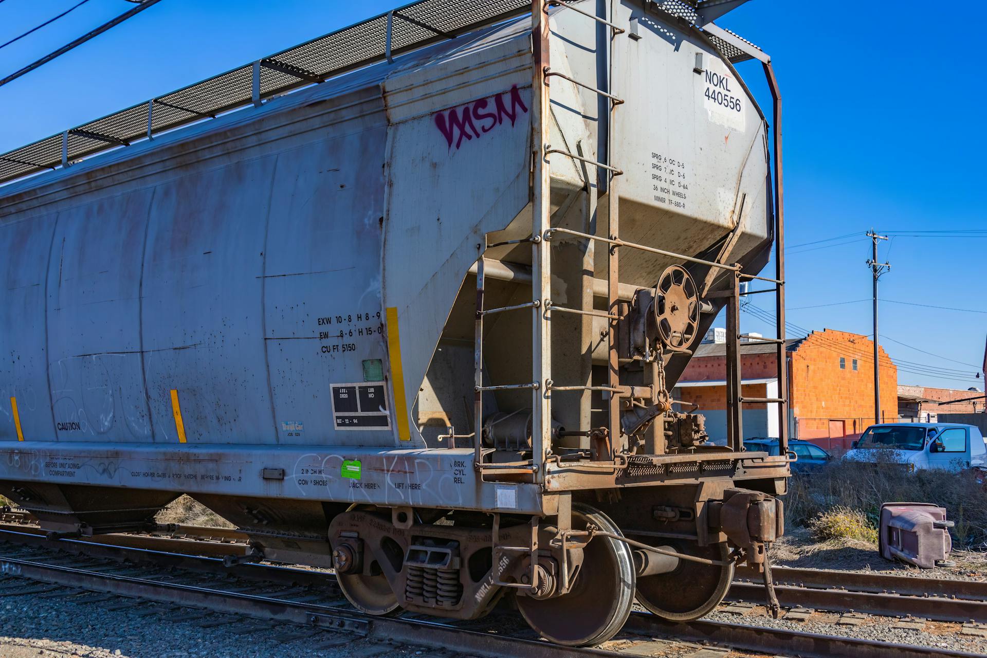 Close-up of a weathered cargo wagon on train tracks under a clear blue sky.