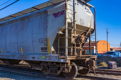 Free Close-up of a weathered cargo wagon on train tracks under a clear blue sky. Stock Photo