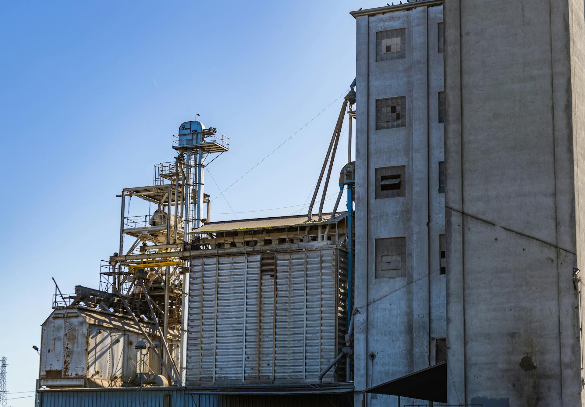 Old factory building with weathered structures, showcasing industrial decay under a bright sky.